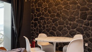 A modern room with a stone wall, a round table, and white chairs. - Dioroh Suites Meteora 303 (Kalabaka)