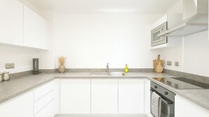 Een moderne keuken met witte kasten, een granieten aanrechtblad, een inbouwoven en een roestvrijstalen spoelbak.