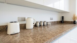 Een moderne keuken met een marmeren aanrecht, een witte broodrooster, een waterkoker en verschillende kleine bakjes.