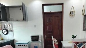 A compact living space with a pink sofa, a matching ottoman, a small kitchenette with a microwave, and a dining area with a white table and chairs.