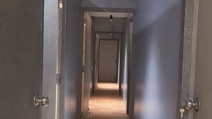 Käytävä, jossa on puulattia ja harmaat seinät, johtaa käytävän päässä olevaan oveen.
