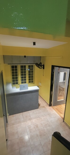 A small kitchen with a grey countertop, a window with a view, and a door leading to another room. - The Loft (Chennai)