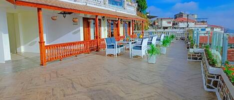 A covered outdoor seating area with wicker furniture and a stone floor.