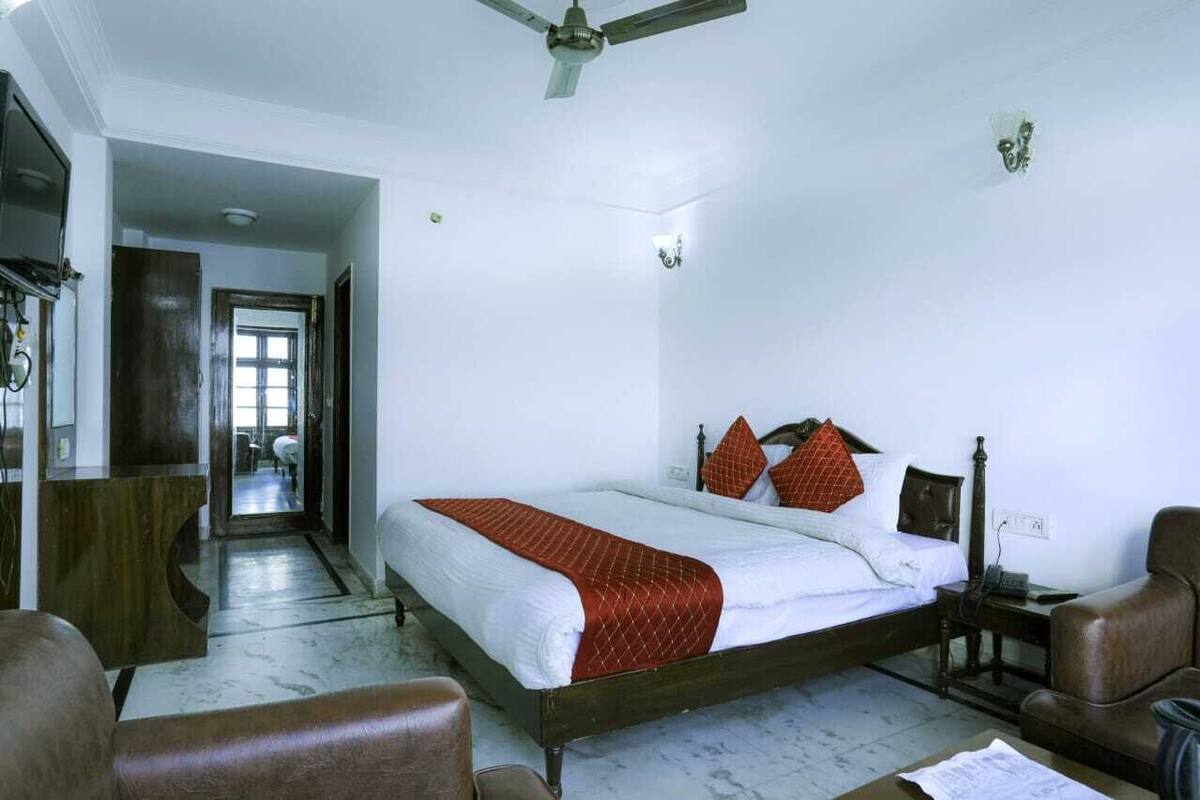 A hotel room with a large bed, a wooden headboard, a desk, and a chair. There is a ceiling fan and a light fixture on the ceiling.