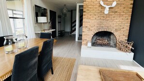 En moderne stue med pejs, træbjælker og et spiseområde med bord og stole.