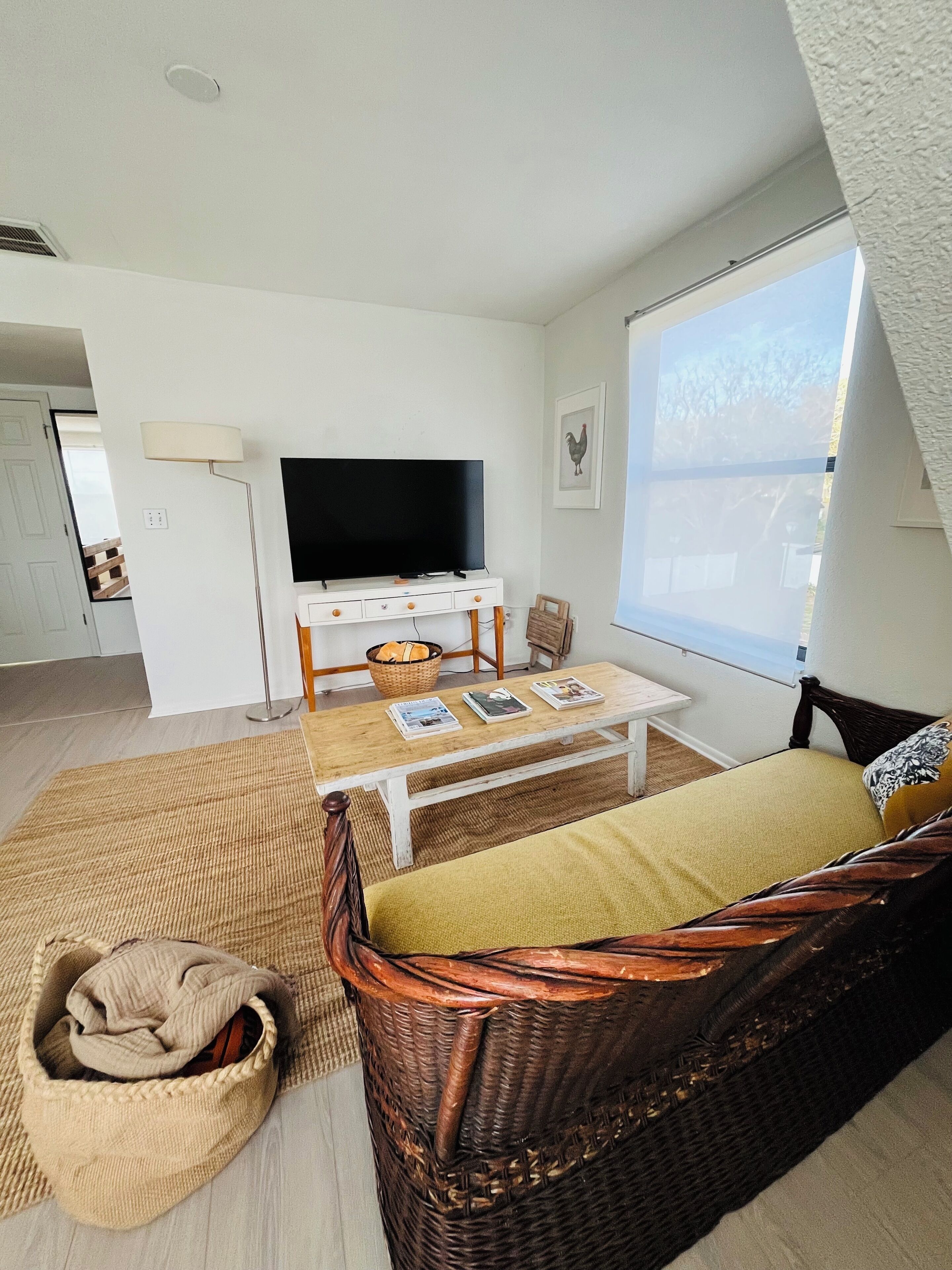 A cozy living room with a television, a dining table, and a wicker sofa.