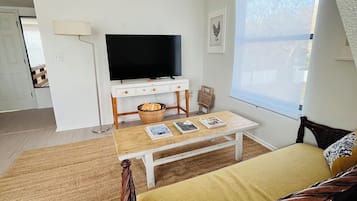 A cozy living room with a television, a dining table, and a wicker sofa.