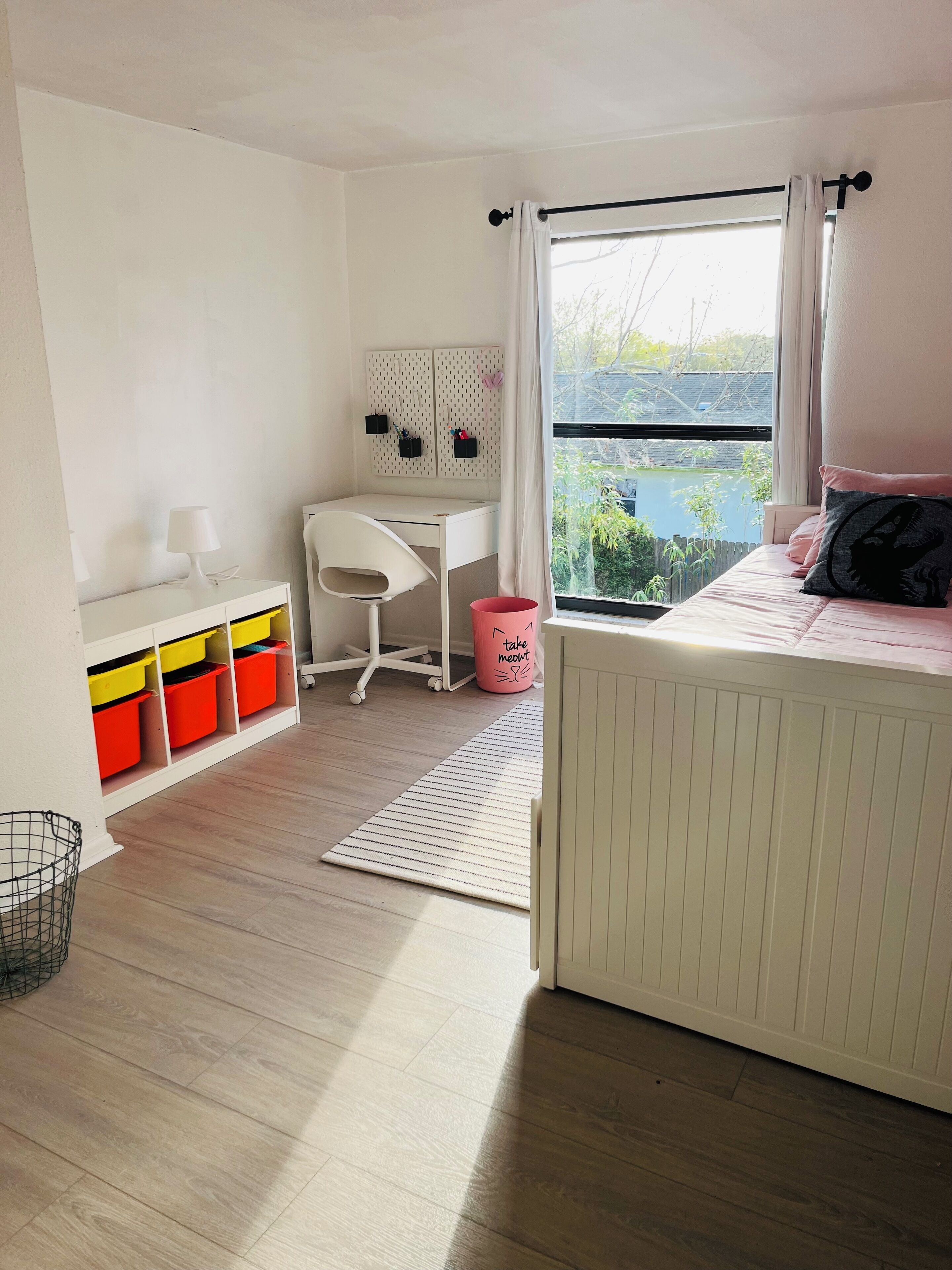 A bedroom with a bed, a desk, a chair, a radiator, a window, and storage units.