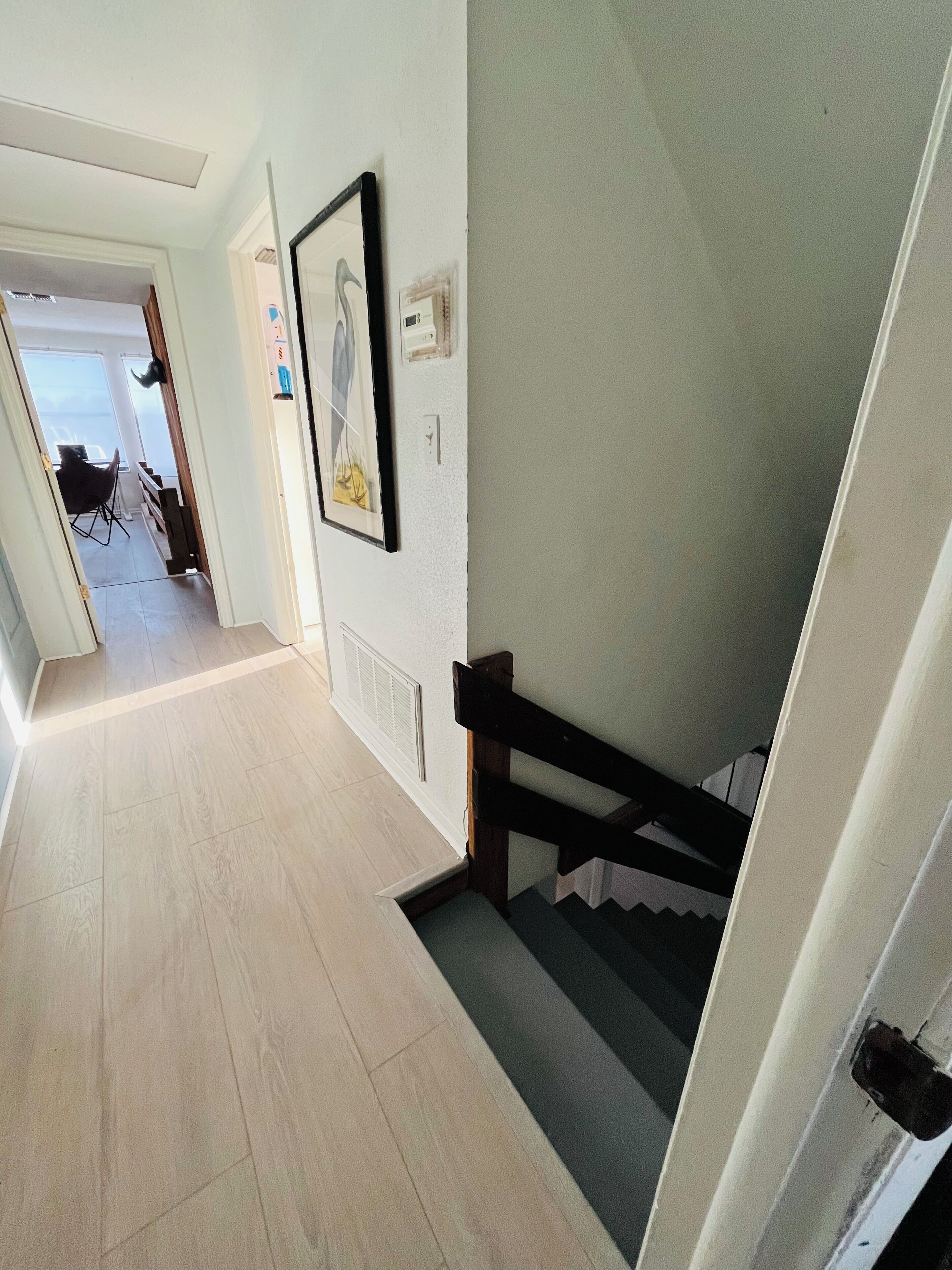 A hallway with a wooden floor, a staircase with a wooden handrail, and a door leading to another room.