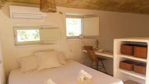 Un dormitorio con cama, dos ventanas, escritorio, silla y cestas de mimbre en estantes.