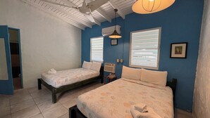 Une chambre avec deux lits, un ventilateur de plafond et une fenêtre avec des stores.