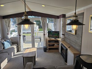 Una sala de estar acogedora con un sofá, una mesa de centro y un televisor sobre un mueble de madera. Hay un balcón con vistas a casas y una terraza.