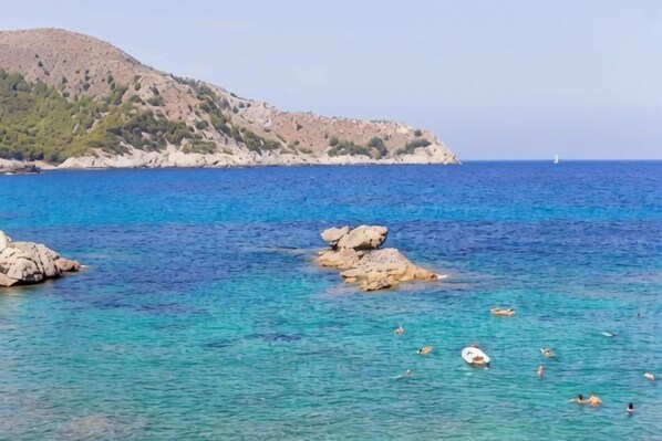 A coastal scene with clear blue water, rocky outcrops, and a hilly landscape in the background. - THB Cala Lliteras - Adults Only (Llevant)