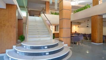 Eine moderne Hotellobby mit einer zentralen Treppe, Sitzbereichen und einer Pflanze auf der oberen Ebene.