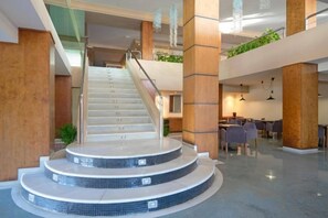 A modern hotel lobby with a central staircase, seating areas, and a plant on the upper level. - THB Cala Lliteras - Adults Only (Llevant)