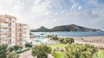 Un hotel con varios balcones, una zona de piscina y vistas al mar y a las montañas.