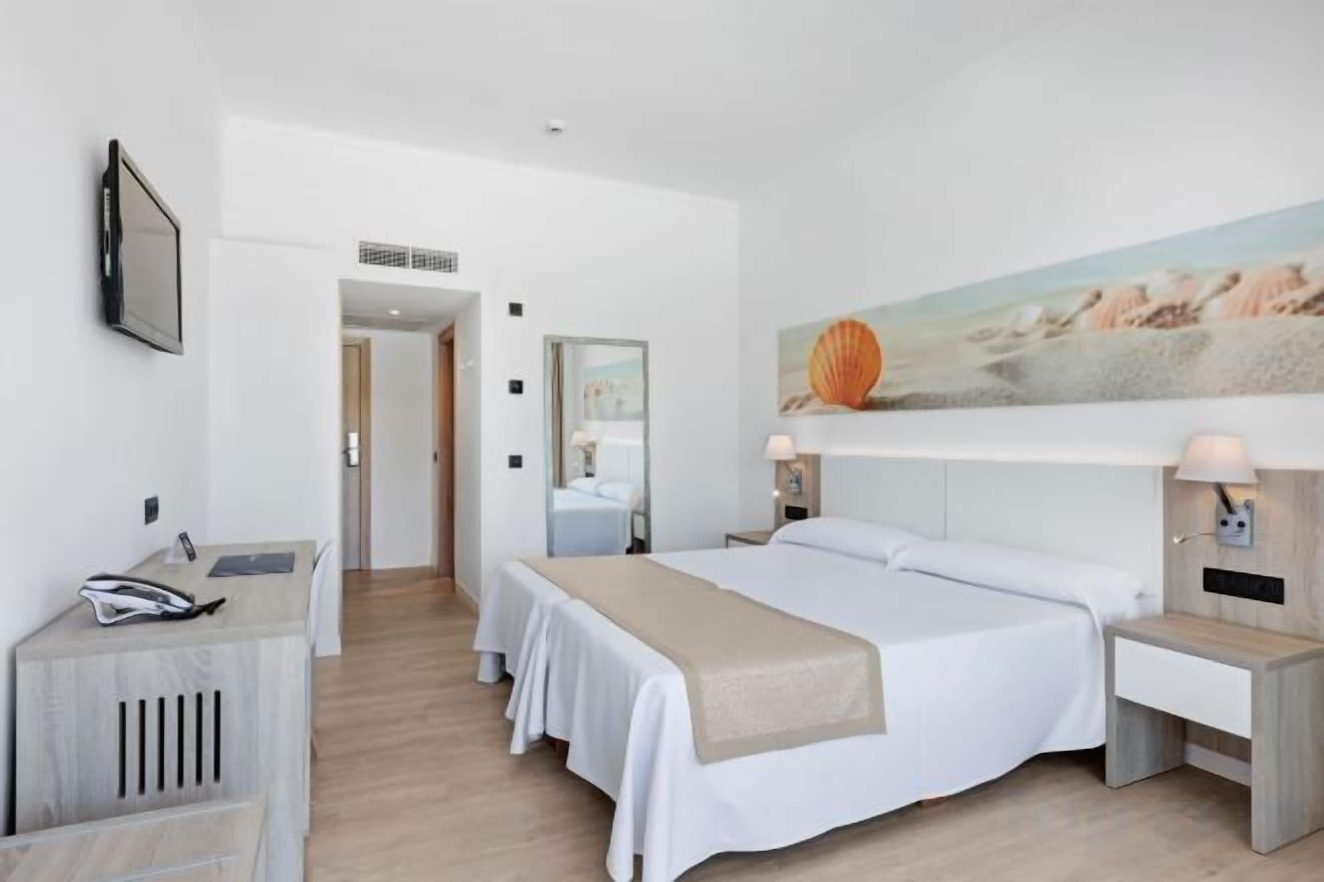 Une chambre d’hôtel avec un lit, des tables de chevet, un bureau et un tableau au mur.