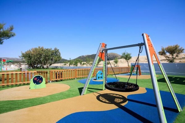 A playground with a swing set and a tire swing, surrounded by a wooden fence and a clear blue sky. - THB Cala Lliteras - Adults Only (Llevant)