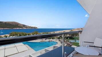 A balcony with a pool, a dining area, and a view of the sea and hills.