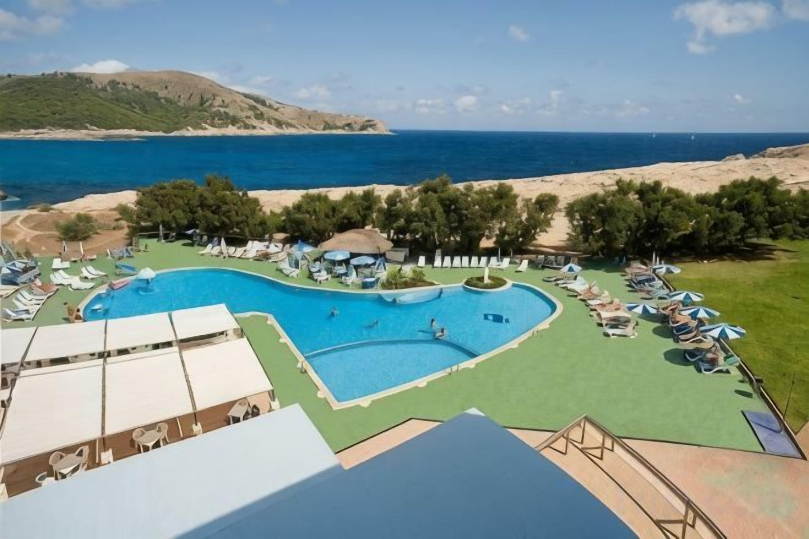Una piscina con vistas al mar, rodeada de sillones y sombrillas.