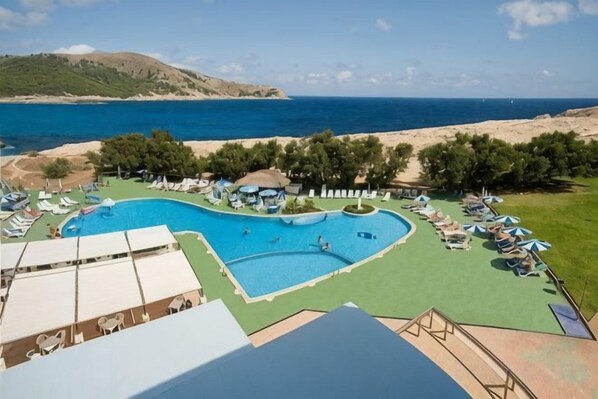 A swimming pool with a view of the sea, surrounded by lounge chairs and umbrellas.