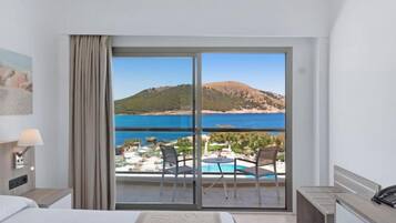 Habitación de hotel con un gran ventanal corredera que da a un balcón y vistas al mar y las colinas.