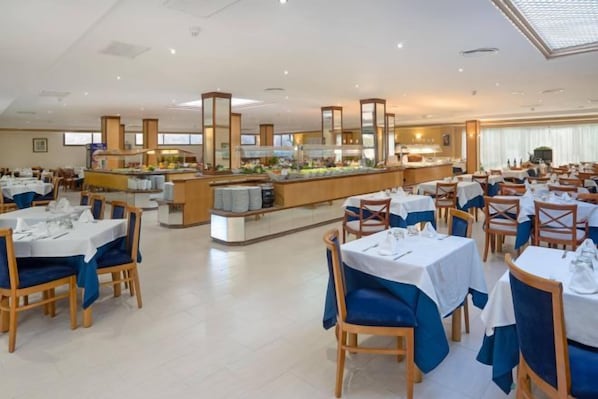 Un vaste espace dédié à la salle à manger, avec de nombreuses tables et chaises, un buffet central et une ambiance lumineuse et agréable.