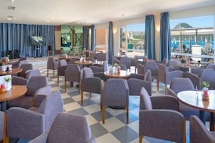 Un comedor de hotel con varias mesas y sillas, ventanas amplias y vistas al exterior.