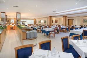 Een ruime eetruimte met meerdere tafels en stoelen, een centraal buffet en een prettige, lichte sfeer.