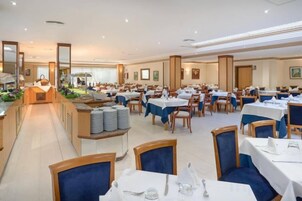 Un comedor amplio con varias mesas y sillas, un bufé central y un ambiente luminoso.