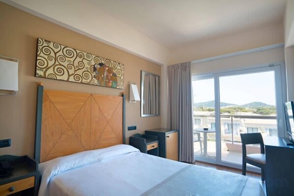 A hotel room with a bed, a desk, a chair, a large window, and a balcony.