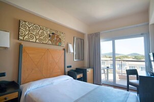 Una habitación de hotel con cama, escritorio, silla, ventana grande y balcón.