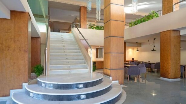 A modern hotel lobby with a central staircase, wooden pillars, and a seating area with tables and chairs. - THB Cala Lliteras - Adults Only (Llevant)