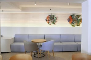 Un intérieur moderne avec un canapé, une table ronde et des chaises, ainsi que deux œuvres d’art représentant des poissons, accrochées au mur.