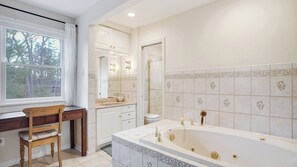 Une salle de bain avec une grande baignoire, un meuble-lavabo avec un miroir et une fenêtre donnant sur les arbres.