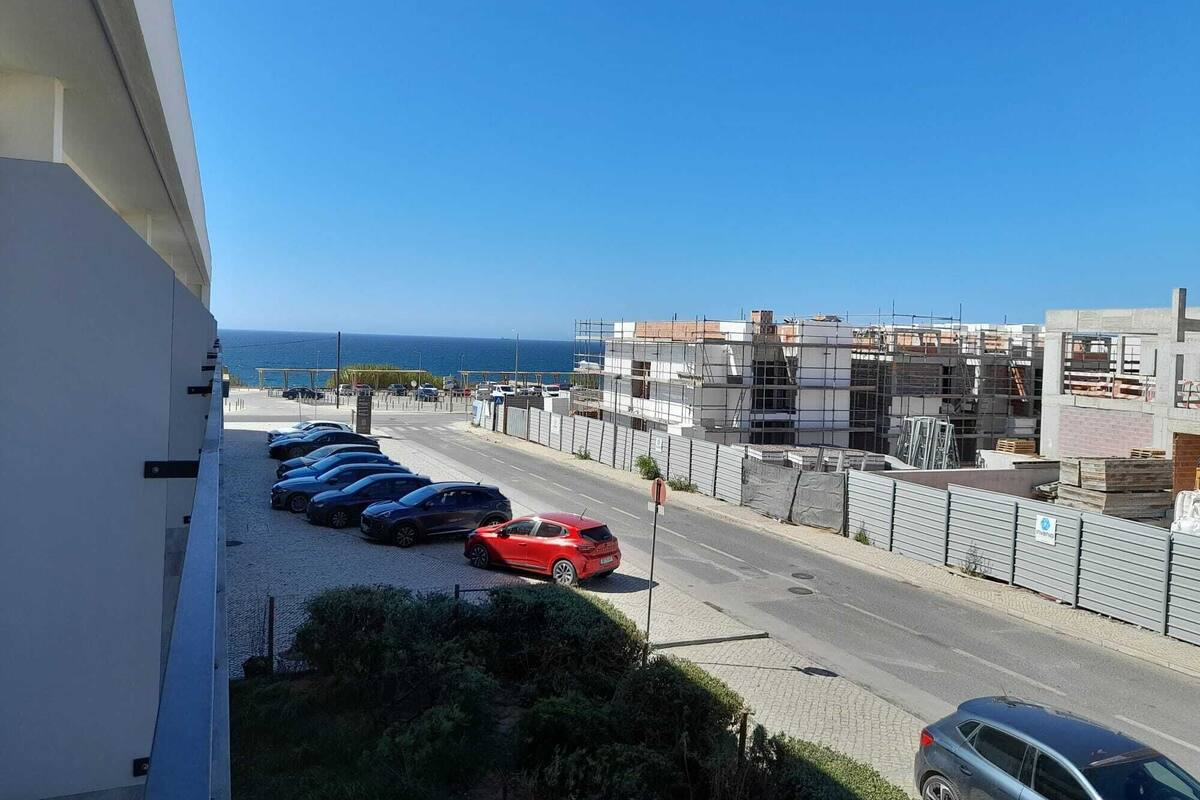 Une route côtière bordée de voitures garées, un chantier de construction et une vue dégagée sur la mer.