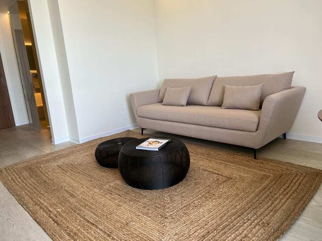 A living room with a beige sofa, two black round coffee tables, and a woven rug.