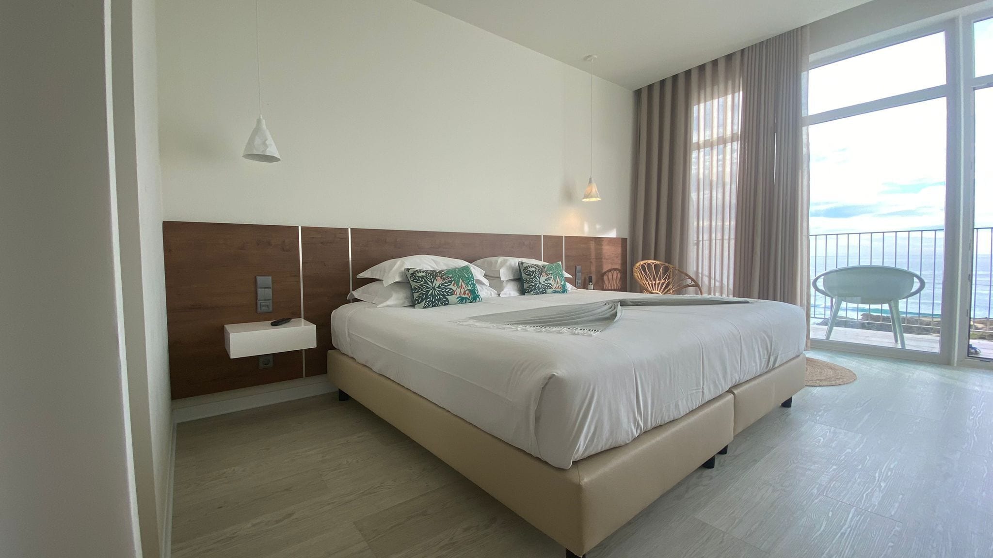 Una habitación de hotel moderna con una cama grande, una mesita de noche con un control remoto, una silla y un balcón con vistas.