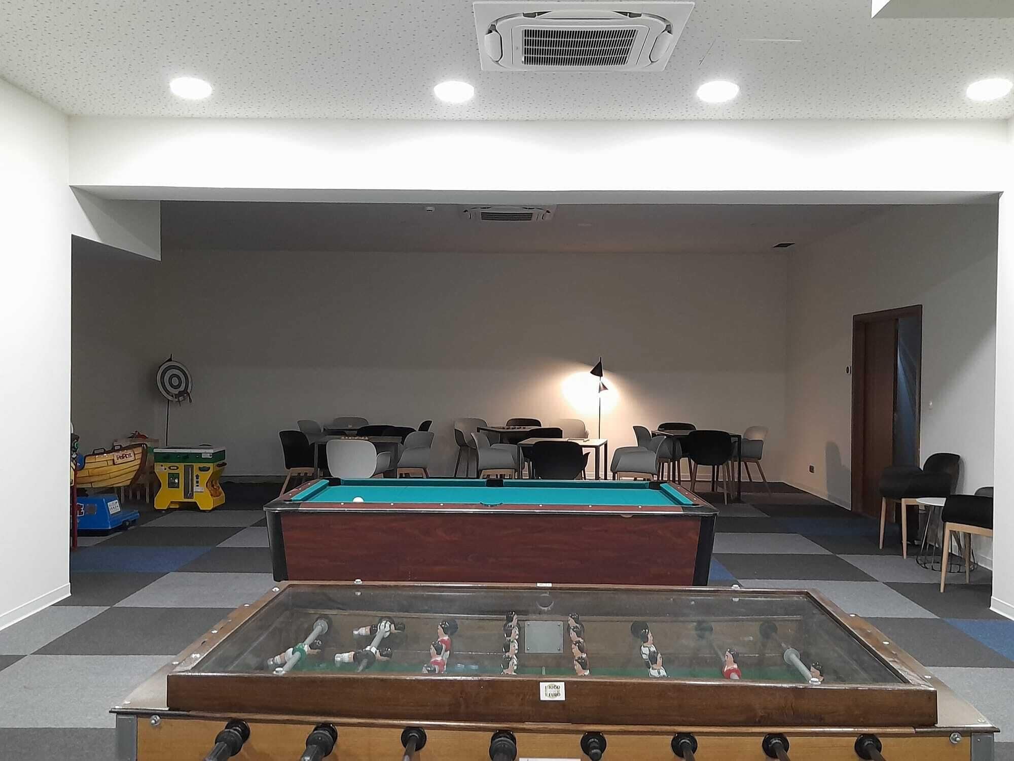 A room with a pool table, foosball table, and several chairs.