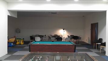 A room with a pool table, foosball table, and several chairs.