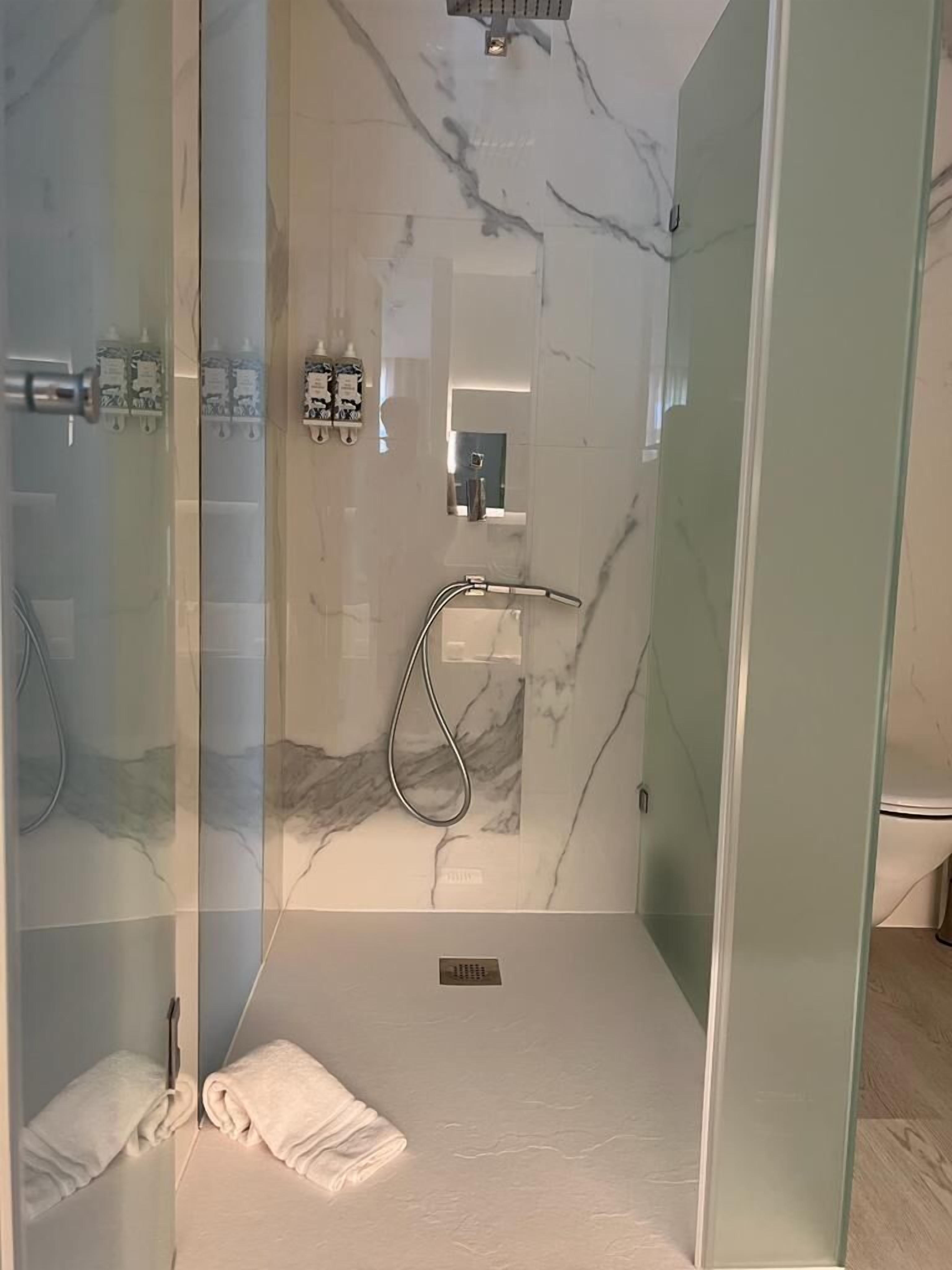 A modern shower room with glass doors, a marble wall, and a visible toilet.