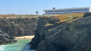 Un bâtiment situé sur la côte, avec une falaise rocheuse et une plage en arrière-plan.