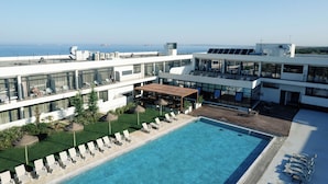 Un hôtel moderne doté d’une piscine sur le toit, de chaises longues et offrant une vue sur la mer.