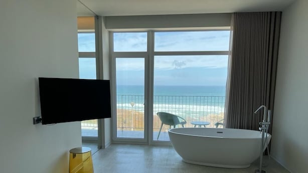 Une chambre d’hôtel avec une grande fenêtre, une baignoire, un téléviseur à écran plat et une paire de serviettes sur le lit.