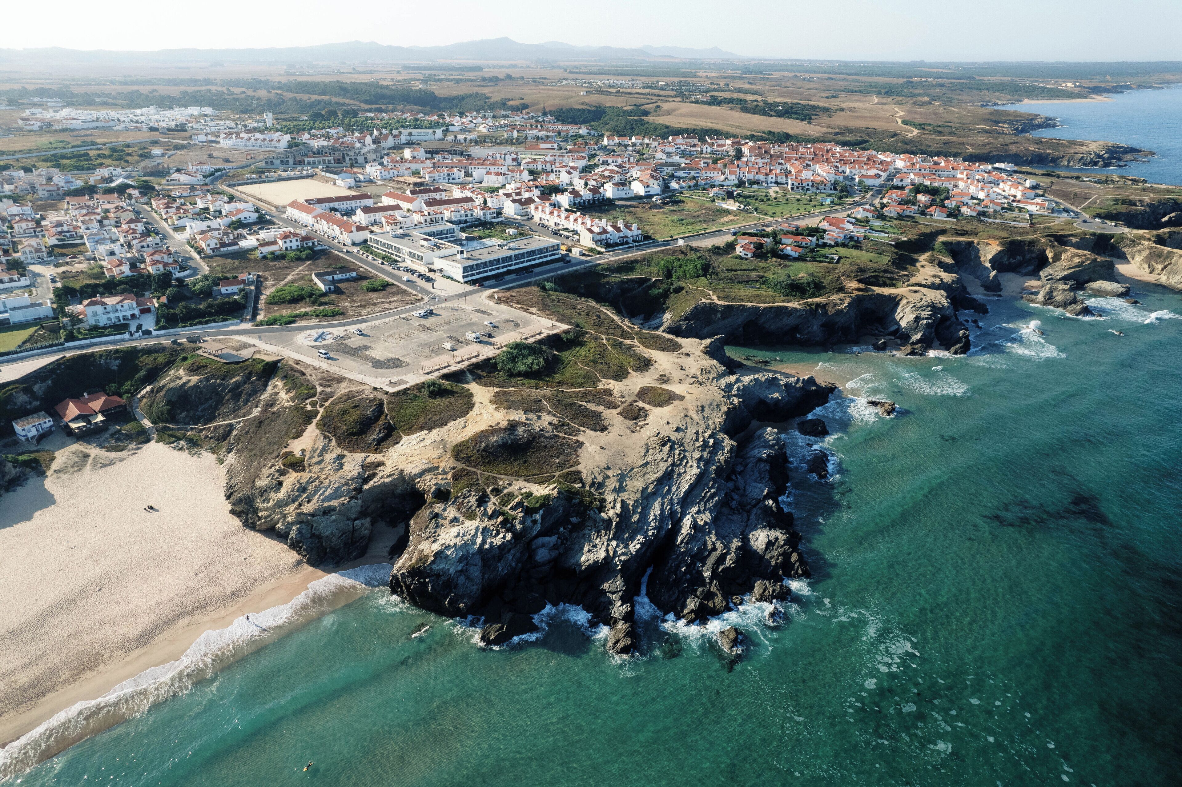 Luftaufnahme einer Küstenstadt mit Strand, felsiger Küstenlinie und Wohnhäusern.
