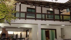 A two-story building with a patio area featuring a brick fireplace, outdoor seating, and satellite dishes on the roof. - MANSION SALE NEW (Europa Belo Horizonte)