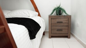A bedroom with a bed, a bedside table, and a potted plant.