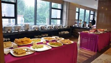 A buffet setup with various food items on tables, a window view, and a room with a carpeted floor.