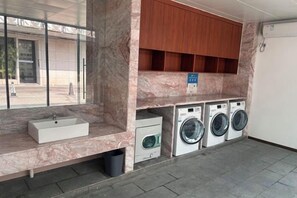 A laundry area with a sink, washing machines, and wooden cabinets. - Xinhaili Hotel (Zhuhai)