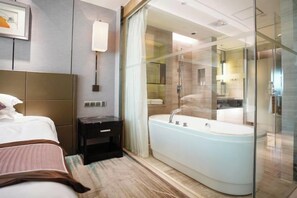 A modern hotel room with a large bed, a small bedside table, a glass-enclosed shower area, and a large bathtub.
